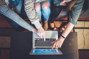 Three people working on a laptop together.